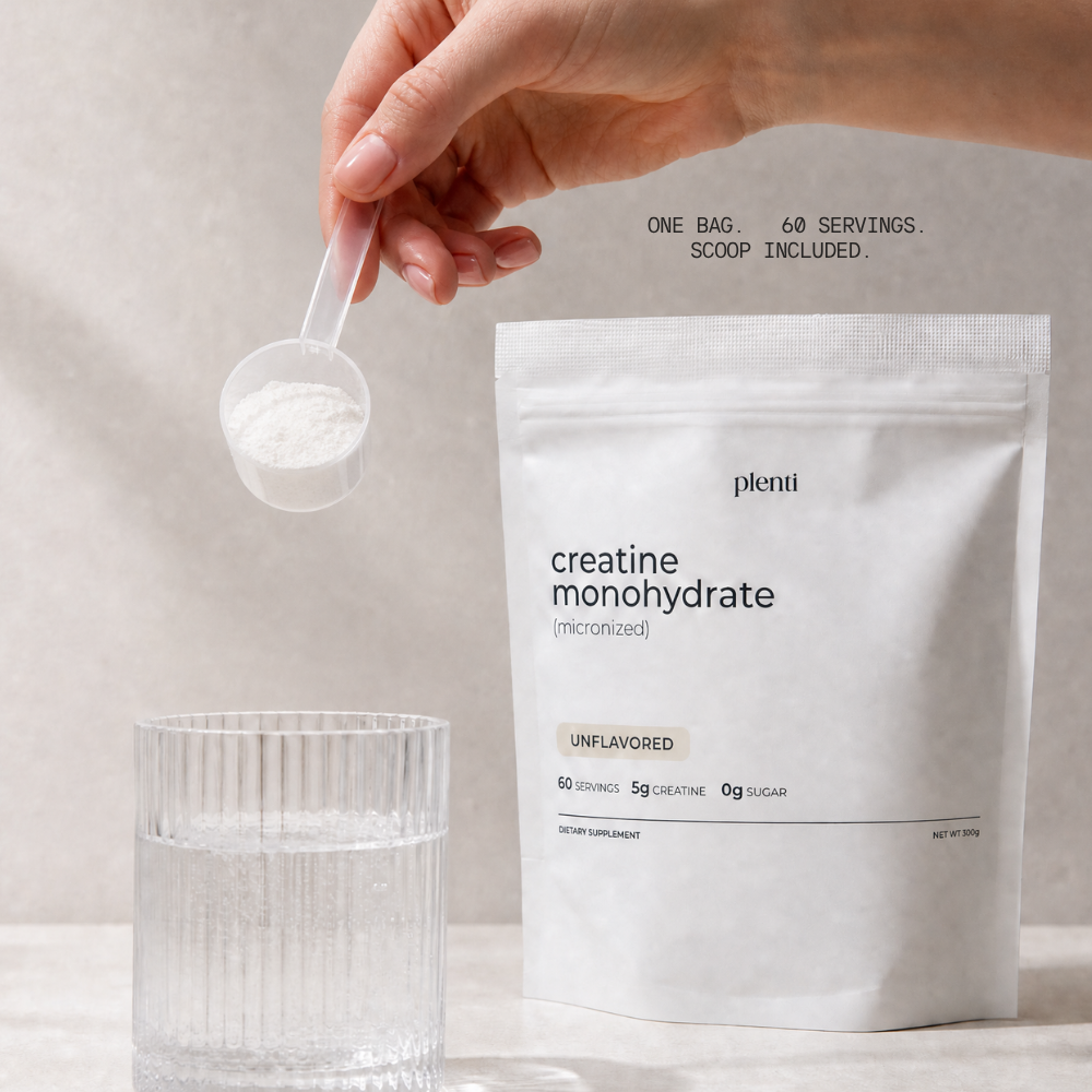 A hand holds a clear scoop filled with white creatine powder above a glass of water, next to a white stand-up pouch labeled 'plent· creatine monohydrate' on a light neutral background.